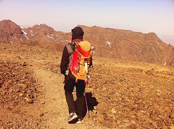 Rear view of man standing on rock against sky