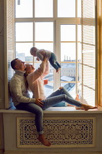 Family in warm sweaters with his son sitting on the window in the winter at sunset