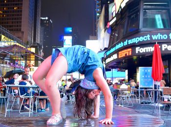 Portrait of young woman bending backwards on city street at night