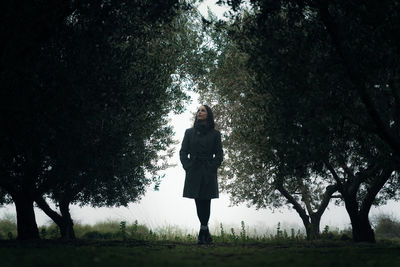 Full length of young woman looking up standing on field in forest