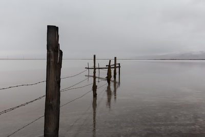 Wooden post in lake against sky during winter