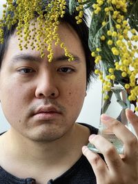 Close-up portrait of young man holding golden wattle flowers in vintage vase.