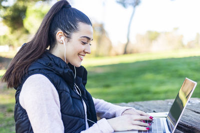 Side view of smiling young woman using mobile phone