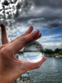 Cropped image of hand holding crystal ball against sky