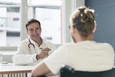 Smiling doctor talking to patient in wheelchair in medical practice