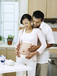 Smiling pregnant woman with man standing at home