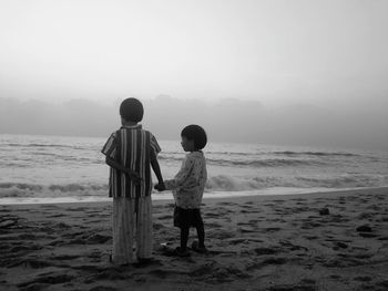 Rear view of boys standing on beach against clear sky