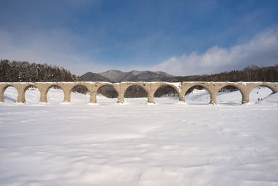 Arch bridge over snow covered landscape against sky