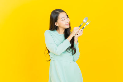 Side view of young woman looking away against yellow background
