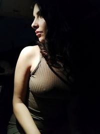 Young woman looking away while standing against black background