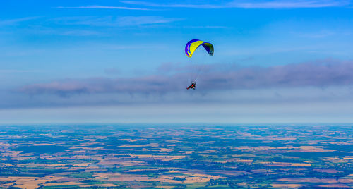 Person paragliding over farm land against sky