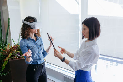High angle view on two standing women in the office, one with vr and another with tablet