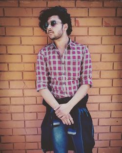 Young man wearing sunglasses standing against brick wall