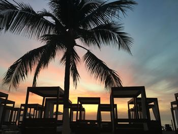 Silhouette palm tree with built structure at beach against sky during sunset