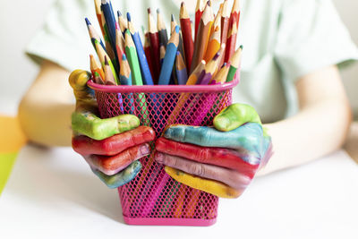 Midsection of boy holding multi colored pencil in desk organizer