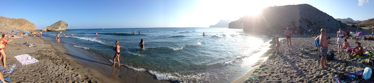 sea, water, beach, horizon over water, shore, large group of people, sand, vacations, leisure activity, clear sky, sunlight, tourist, lifestyles, scenics, panoramic, tourism, beauty in nature, wave, mixed age range