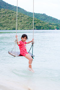 Full length of little girl on swing in sea