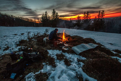 Man with dog sitting by bonfire on land during winter
