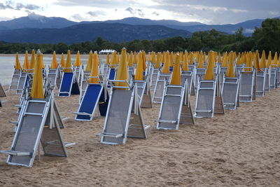 Deck chairs and yellow parasols at beach against sky