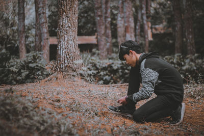 The view from the side of a man tying his shoelaces in the forest