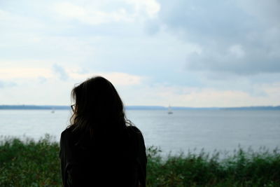 Rear view of woman standing at beach against sky