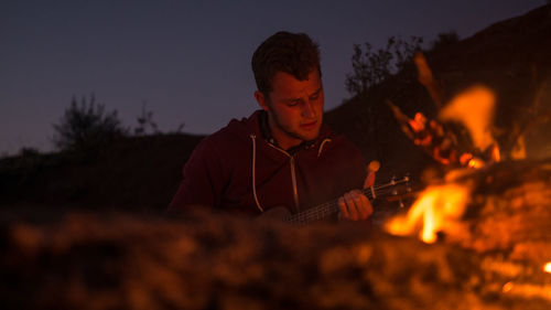 Man playing guitar by campfire at night