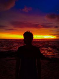 Silhouette man standing on beach against sky during sunset