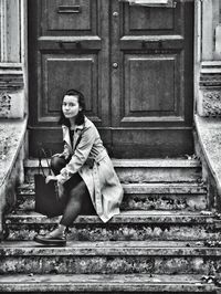Portrait of young woman sitting by door on steps