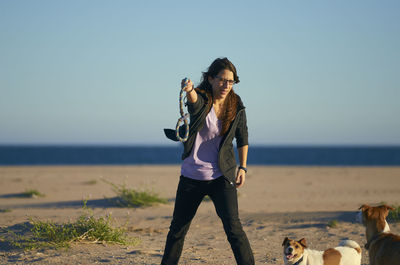 Woman playing with dogs at beach against blue sky