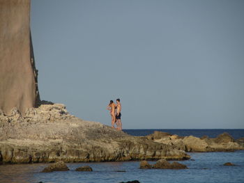 Couple standing by sea against clear sky