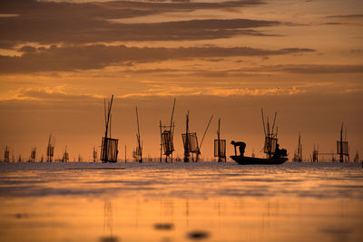 Silhouette men on sailboat in sea against sky during sunset