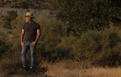 Portrait of adult man in cowboy hat standing in field during sunset