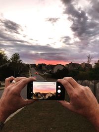 Close-up of hand holding camera against sky during sunset