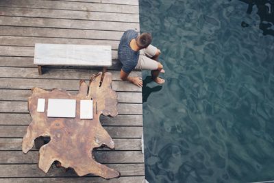 High angle view of young man sitting on pier over lake