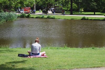 Rear view of woman sitting on grass field by lake