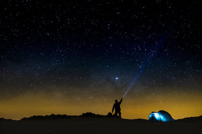 Silhouette man with flashlight against star field at night