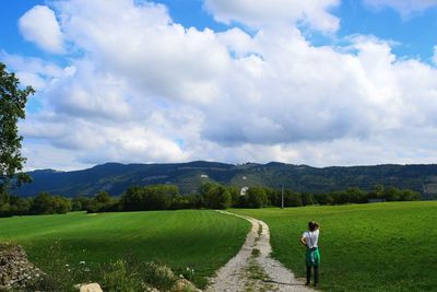 Rear view of man standing on grassy field against cloudy sky