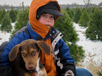 Portrait of boy embracing dog while sitting on snowy field