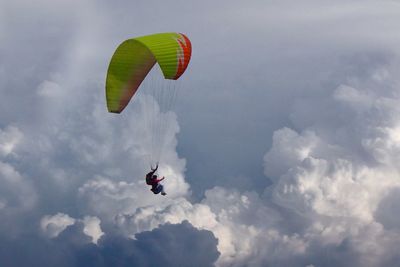 Low angle view of person paragliding against cloudy sky