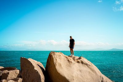 Man standing on rock by sea against sky