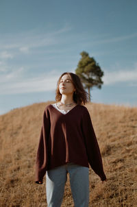 Young woman standing on field against sky