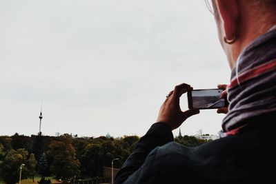 Midsection of man photographing with mobile phone against sky