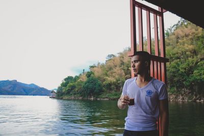 Man having drink while standing by lake