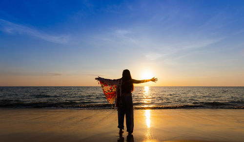 Rear view of woman standing at beach during sunset