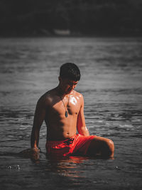 A photo of a  shirtless man bending in the water and looks wet.