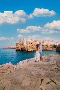 Rear view of women on rock by sea against sky