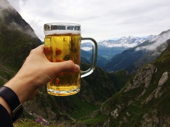 Close-up of hand holding beer glass against mountain range