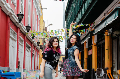 Full length portrait of smiling young woman standing against buildings