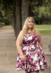 Beautiful young woman standing on road against tree trunk