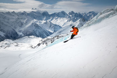 A skier in bright sports equipment goes down the glacier against the backdrop of a cloudy sky and